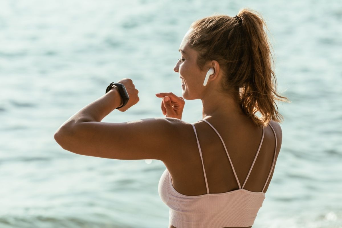 femeie zambind in timp ce se uita la smartwatch inainte de alergarea pe plaja